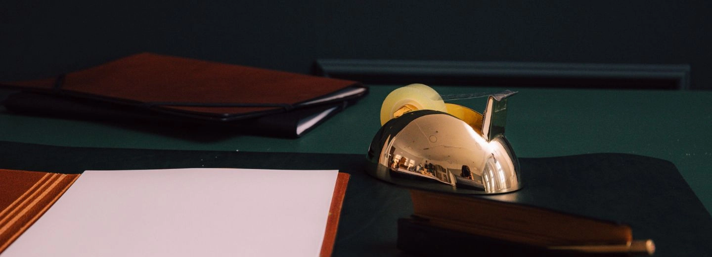 Schreibtisch mit goldenem Tischabroller, Notizbuch und Schreibunterlage in dunklen Tönen